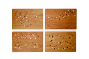 Four equal-sized cutting boards in medium wood with visible woodgrain are each decorated with a different formation of the same dot pattern.
