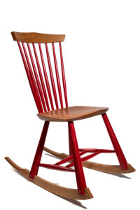 Angular, armless, wooden rocking chair with red back slats and red legs.