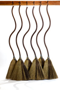 A line of six brooms hanging from wooden pegs each with long squiggle-shaped handles.