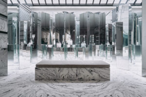 A mirrored retail interior showcasing sculptural displays of handbags on glass pedestals above a marble base.