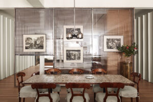 A refined dining room with a long stone table, carved wooden chairs, framed artworks, and glass partition walls.