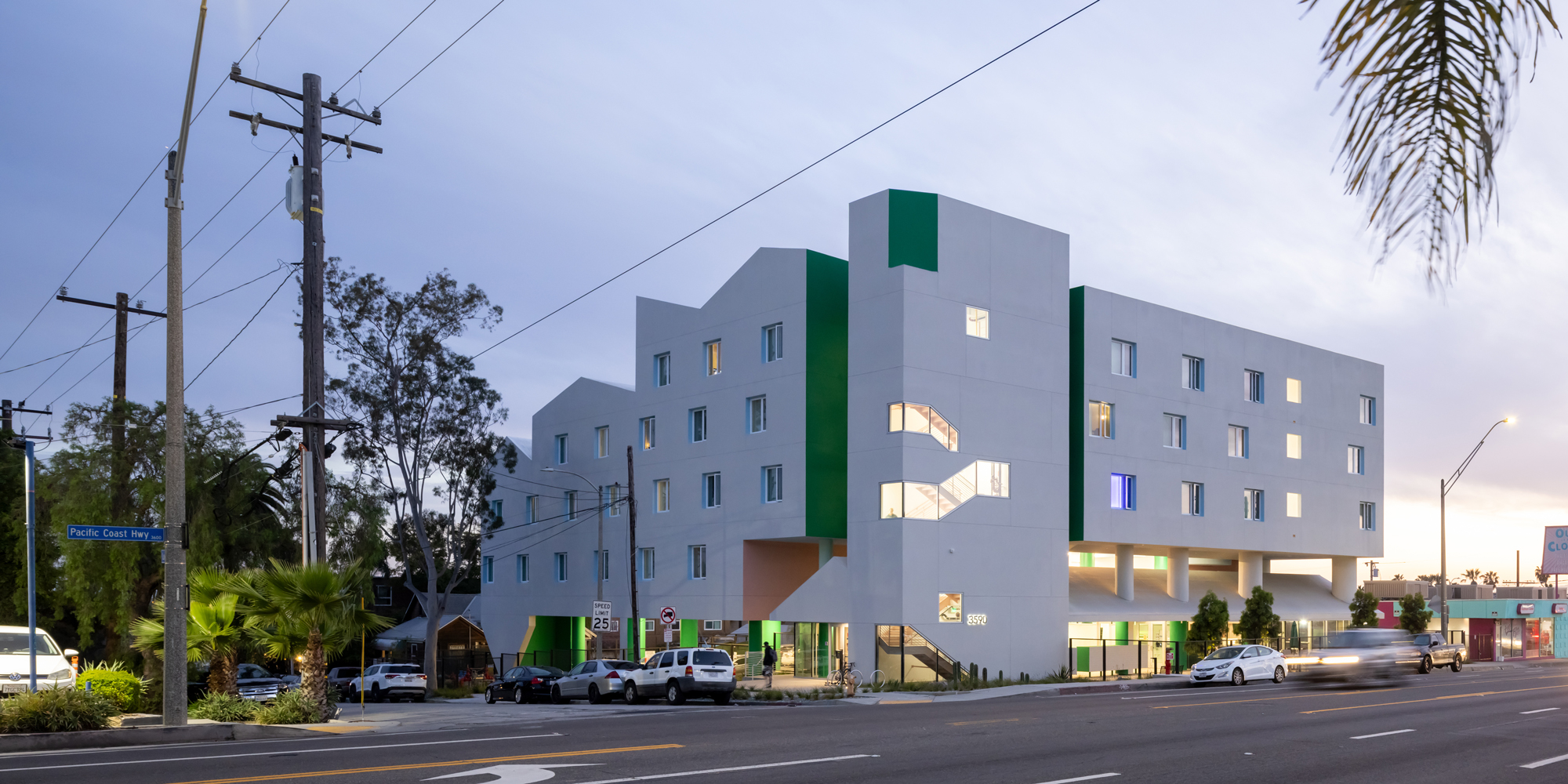 Facade of a modern white building at dusk with an undulating triangular roof and decorated with accents of dark green.