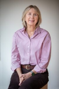 Person wearing a light purple button down shirt seated on a stool.
