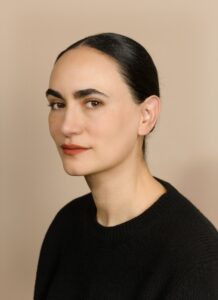 Person in a black sweater posed against a plain beige background in studio lighting.