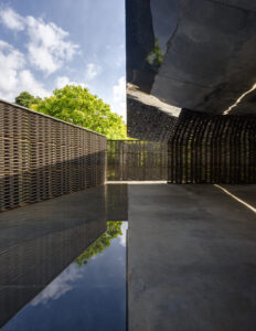Dark brown metal pavillion with rectangular reflecting pool.