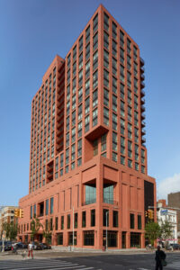 A towering terracotta colored building with smartly-placed cutouts and lush rooftop greenery.
