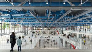 Digital rendering of a sprawling, industrial, open three-story lobby of Centre Pompidou lined with glass walls and exposed metal armature.