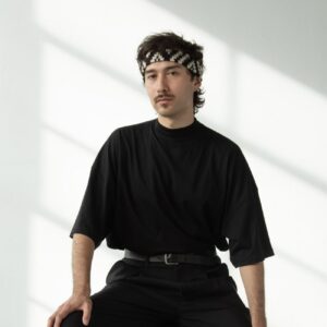 A person in black clothing sits in a white room with natural lighting.