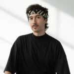 A person in black clothing sits in a white room with natural lighting.
