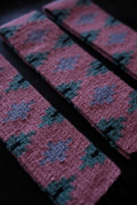 An up close detailed image of three strips of geometric woven textiles. The textiles are pink, blue, and purple.