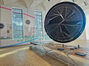 Room with a long table under a large suspended black circle with a white ring and lines crossing and twisting