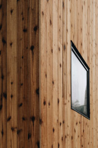 Exterior of a wood paneled side of a house with square window.
