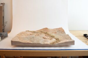 Carved wooden topographical model of Rancho Almosomos with visible wood grain and grooves.
