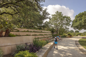 Outdoor greenspace featuring a multi-tiered stone fountain that stretches along a wide walkway surrounded by towering trees.