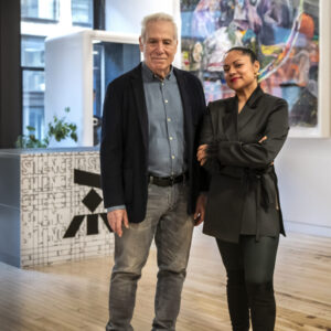Two people standing in a bright art-filled room with wooden floors and colorful artwork.