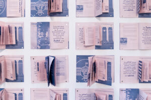 A series of open pink and blue booklets tacked onto a wall.