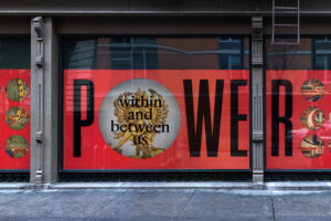 A bright red advertisement banner along street-facing windows that reads "Power" in a human-size font, and within the "o" in smaller font are the words "within and between us".
