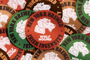 A pile of overlapping discs in red, green, tan, and brown that all display an illustration of a wolf hound and display the words "New York brewed/ Irish Ingenuity".