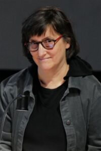 Person in dark layered clothing wearing dark rimmed eyeglasses.