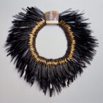 Ornate, avant-garde necklace made of bent nails with an iridescent central element surrounded by gold-toned spikes and black feather-like extensions.