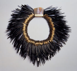Ornate, avant-garde necklace made of bent nails with an iridescent central element surrounded by gold-toned spikes and black feather-like extensions.