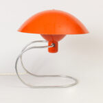 Umbrella shaped orange lamp held by slim curving steel c-shaped platform creating the illusion that the lamp is floating.