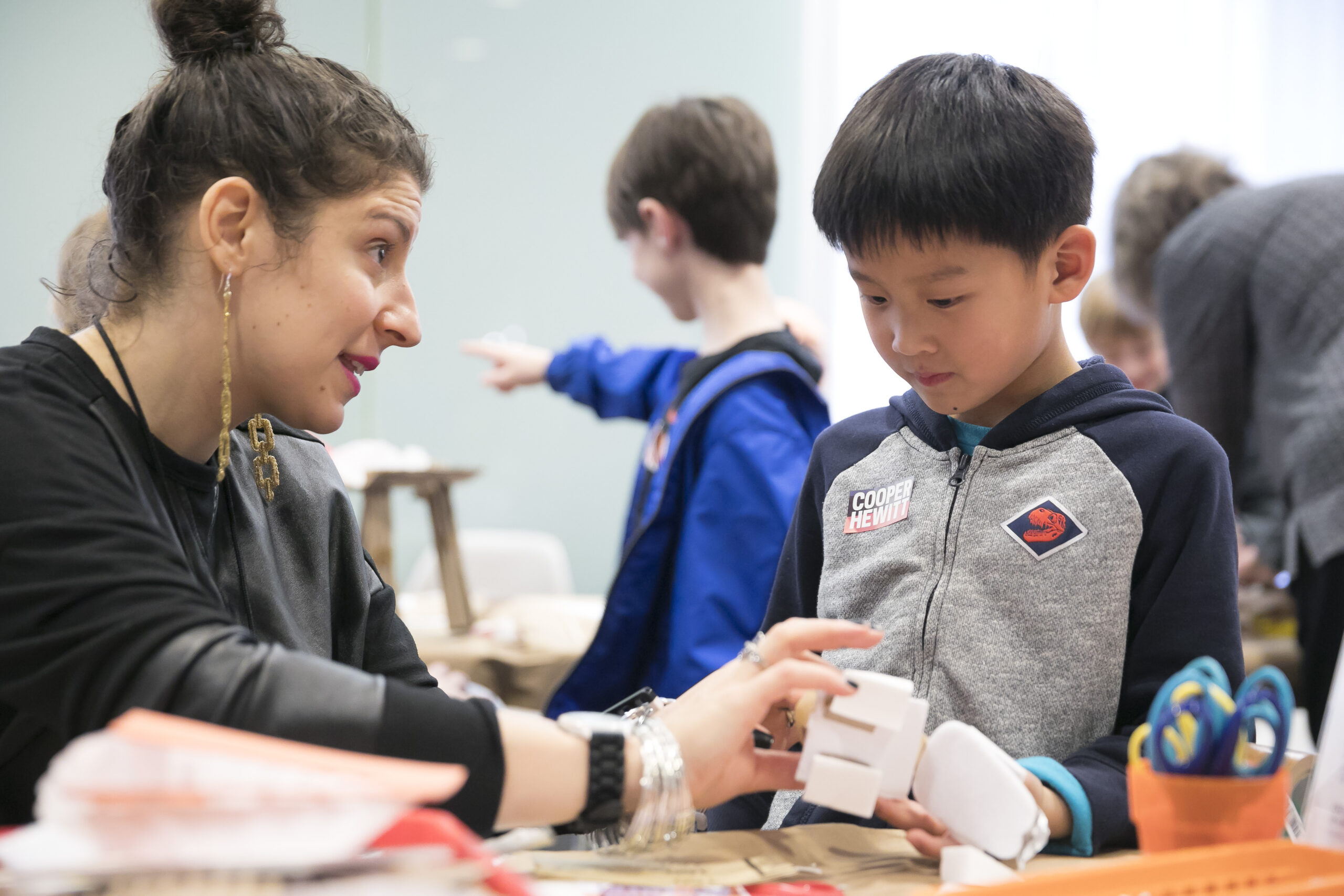 Museum educator talking to and assisting a young child who is making something three-dimensional