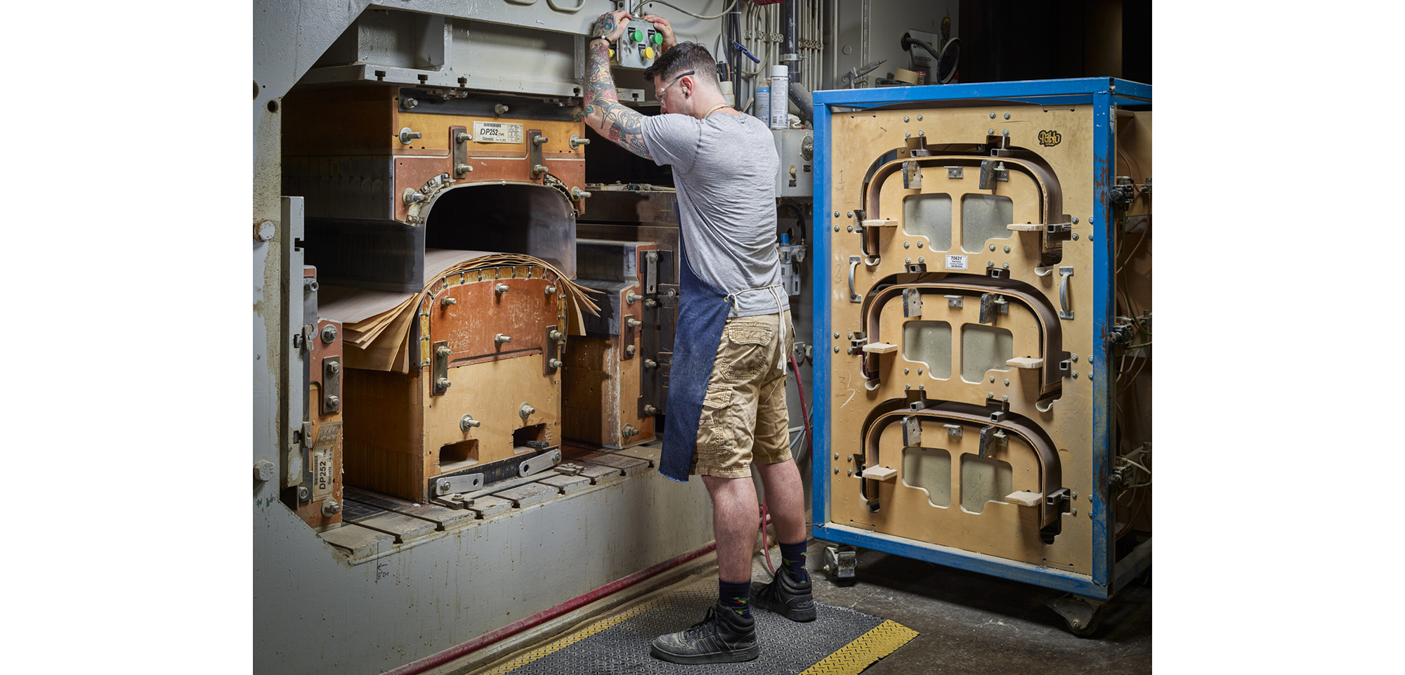 Person operating industrial press with stacked material sheets in workshop.