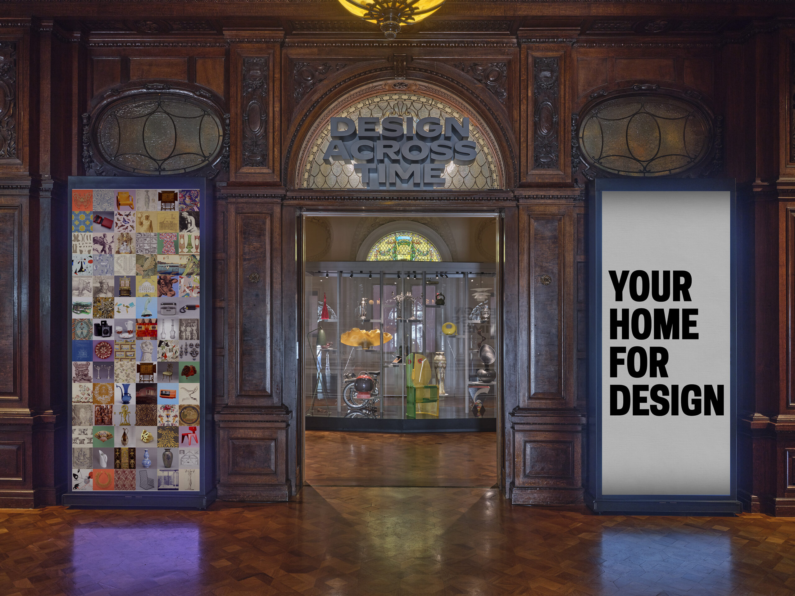 Two digital totems frame the entryway to a gallery with a center case. A metallic sign that reads "Design Across Time" sits above in the archway. The walls and floors are wood, carved with artisanal detail.