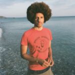 Portrait of person in orange shirt in front of a body of water.