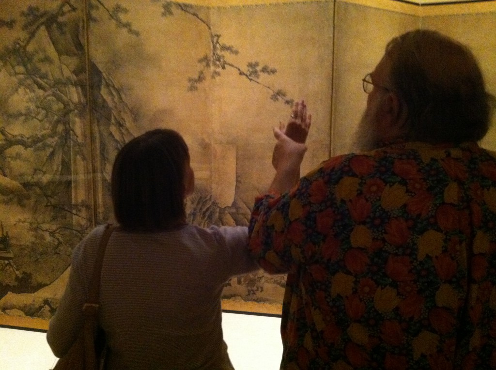 Dave & Linda standing with their backs to us, facing a beige and black painting.. Dave has Linda's hand in his, and is holding it outstretched.