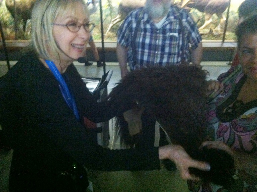 Irene is holding an approximately two foot by one foot swatch of bison fur in both hands, grinning as she holds it out for others to feel.