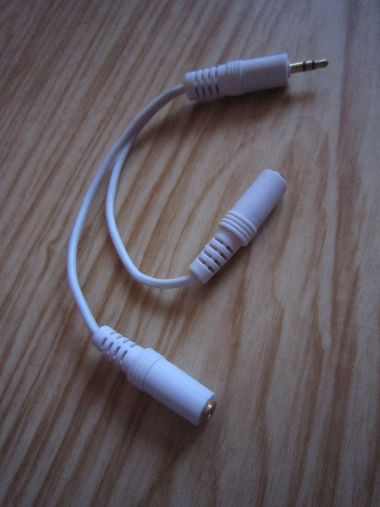 A white cable with one 3.5mm male audio jack plug connected to two 3.5mm female jacks.