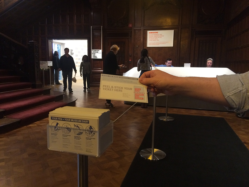 a person's hand pulling a postcard out of an acrylic stand which holds a stack of cards. the setting is a darkened lobby.